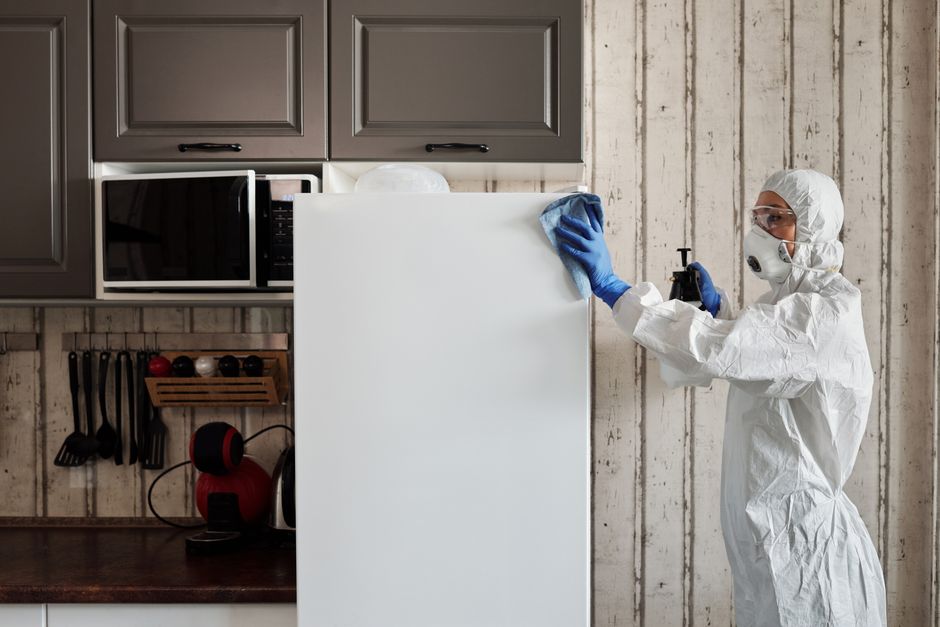 Person in protective gear sanitizing kitchen surfaces with disinfectant.
