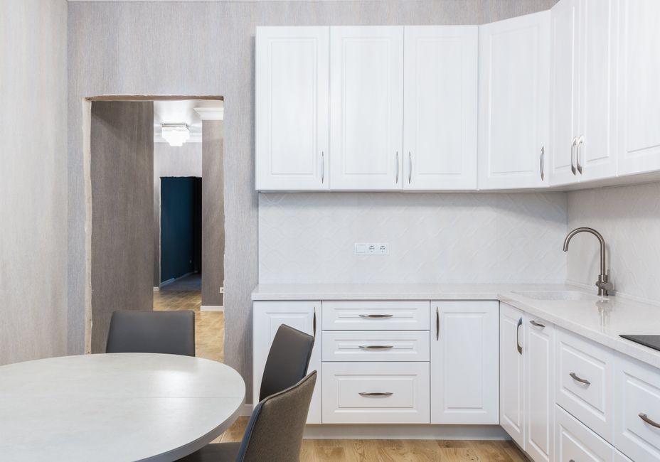 Contemporary kitchen interior with white cupboards and tap against table with chairs on parquet in light house
