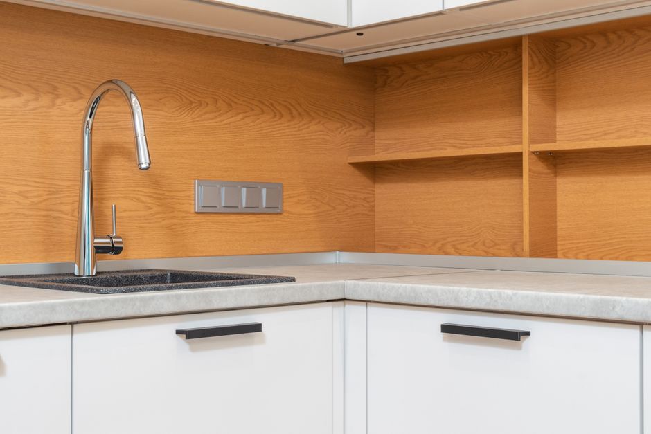 Wooden shelves and switches above table with cabinet and stainless steel tap in modern house kitchen